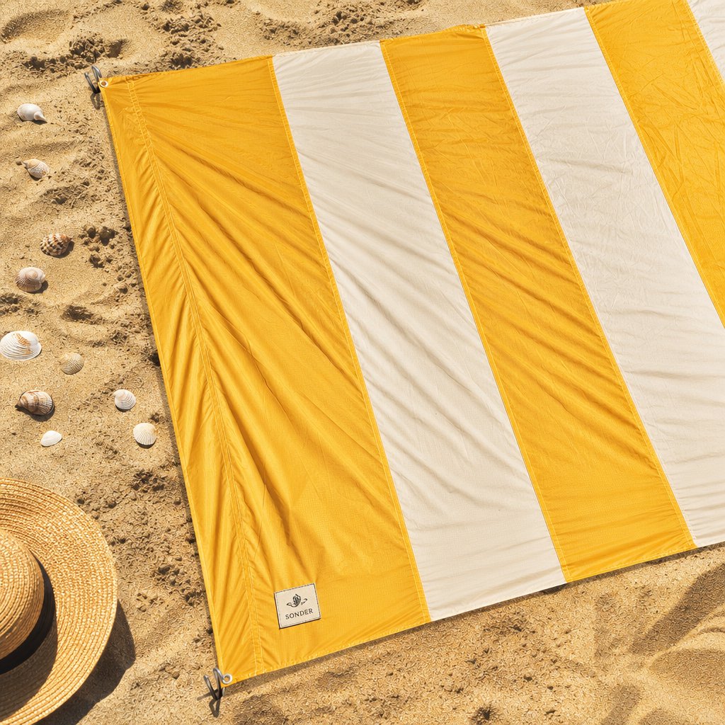 Oversized sand-free beach blanket in ochre and cream stripes spread on golden beach sand