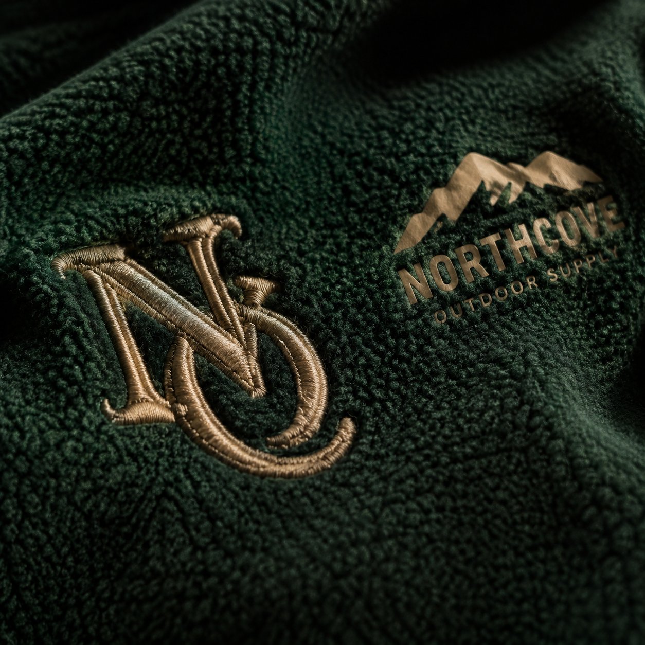 Macro of an embroidered monogram beside a screen-printed logo on a forest-green fleece blanket