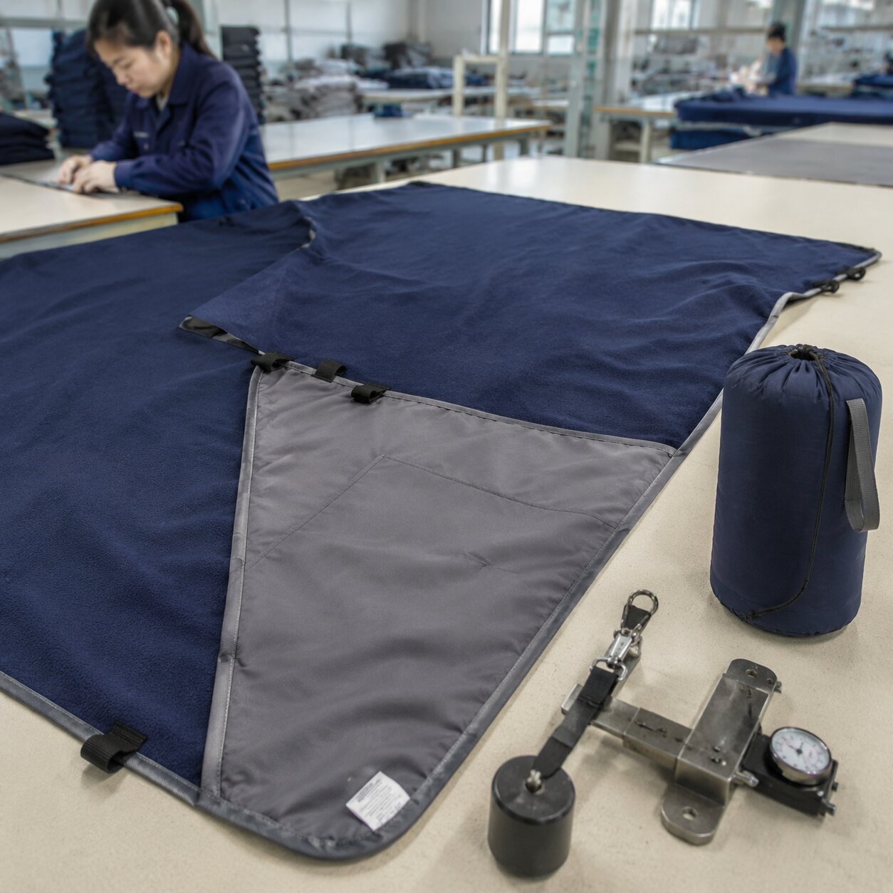 Reversible camp blanket showing navy microfleece face, grey polyester pongee reverse, corner pocket, wind clips, seam gauge and stuff sack